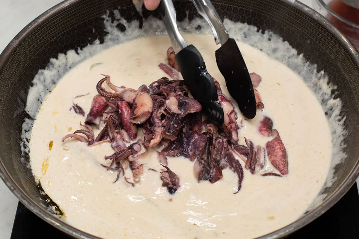 Adding the cooked squid into the simmering coconut milk in a wok.