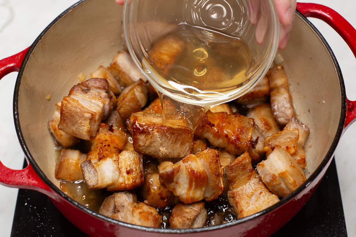 Adding vinegar to the meat in the pot.