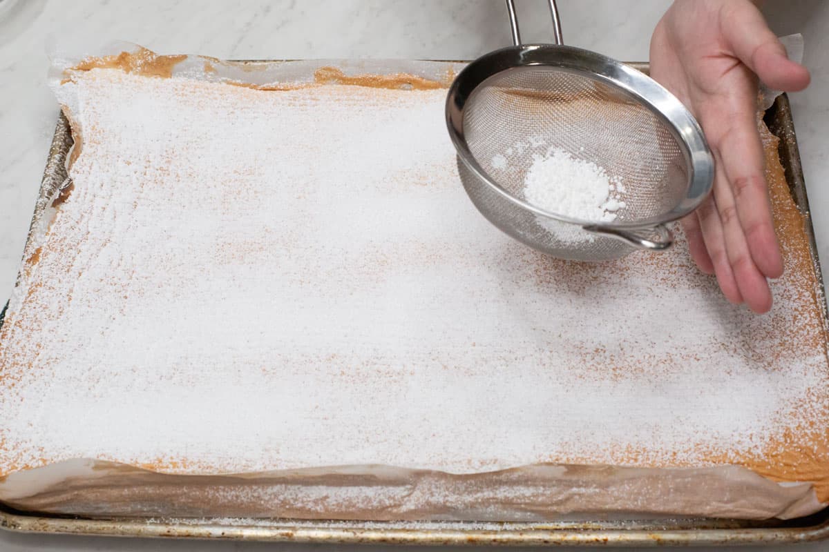 Sprinkling a generous amount of powdered sugar over the baked meringue using a strainer.