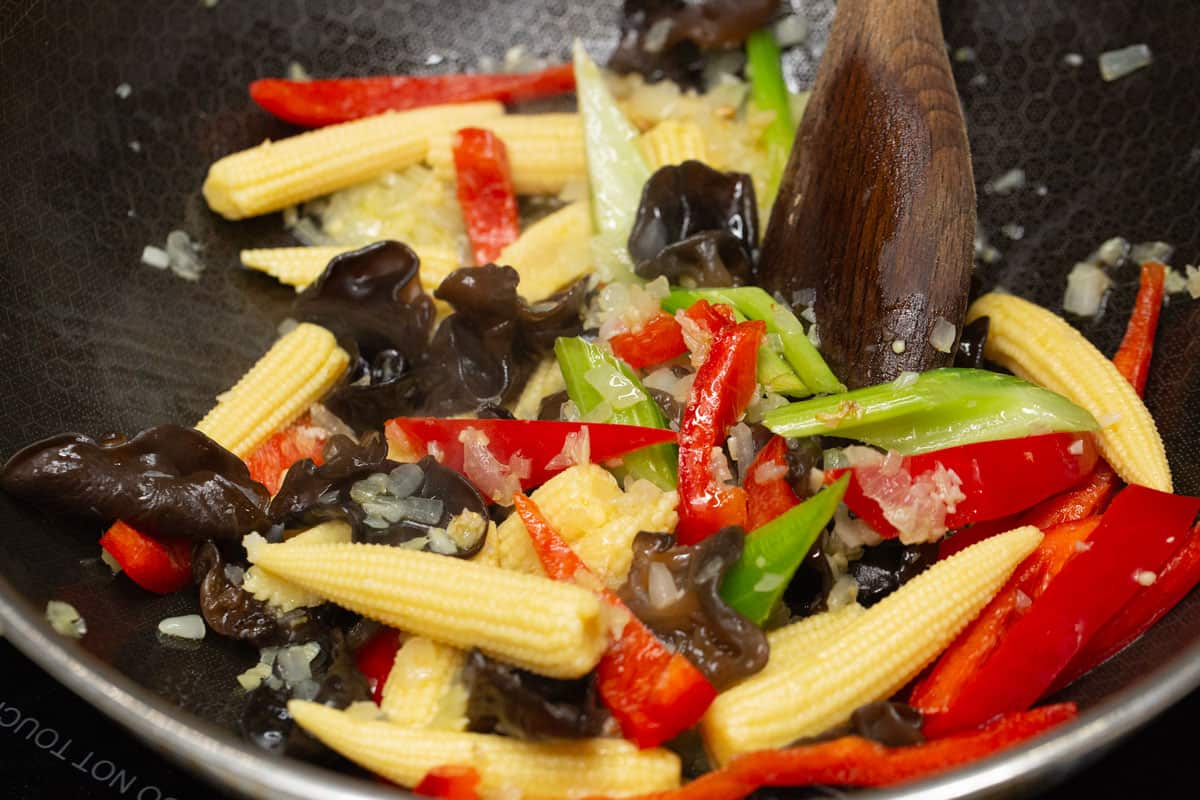 Stir-frying mushrooms, baby corn, red bell pepper, and celery in a wok.