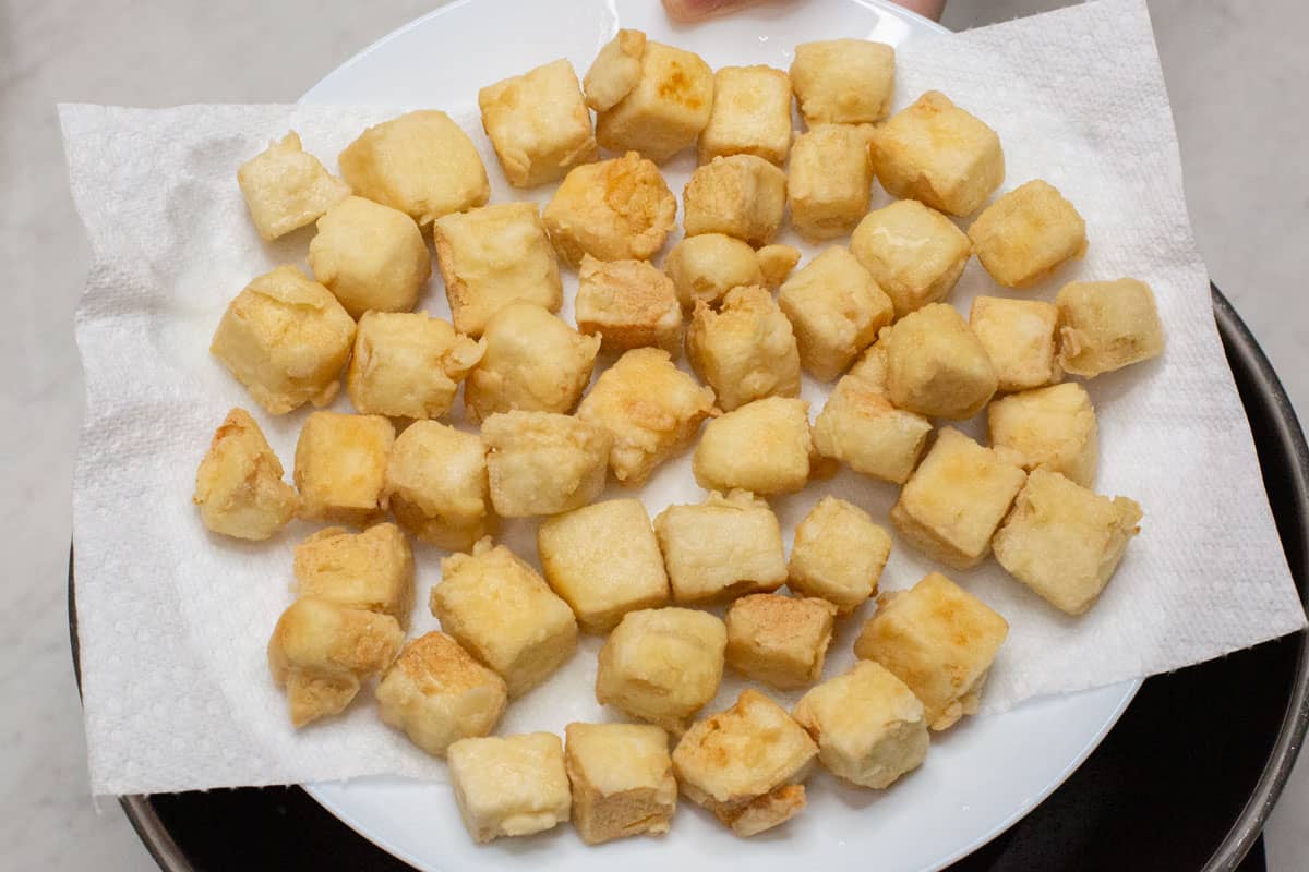 Fried tofu pieces on a paper towel-lined plate.