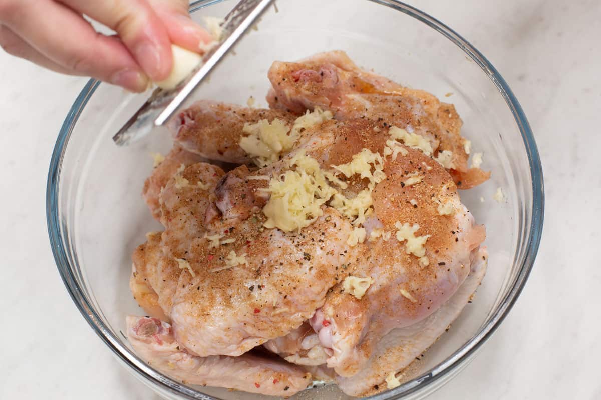 Grating garlic over the bowl with chicken wings and seasonings.