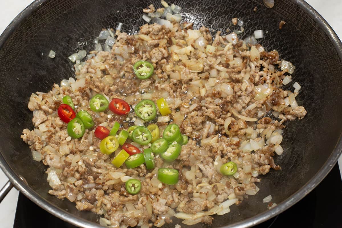 Sauteing the aromatics and pork with the chilies in a wok.