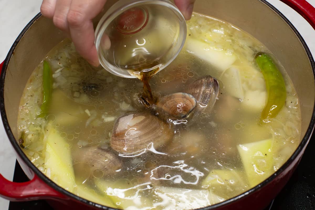Adding the fish sauce into the pot of Filipino Clam Soup (Tinolang Halaan).