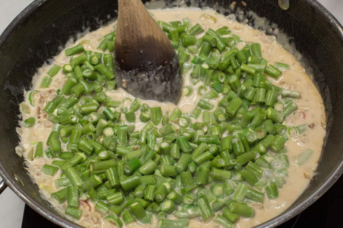 Adding the green beans in the coconut mixture in the wok.