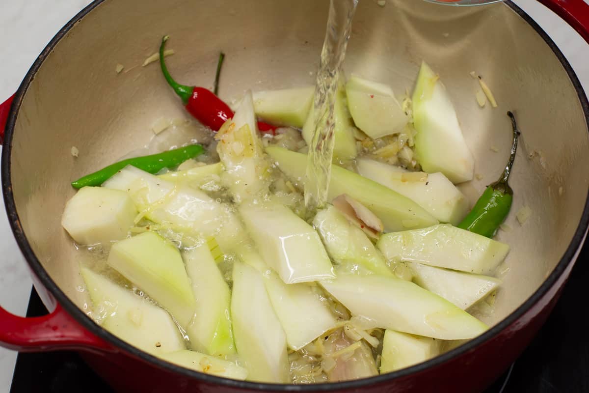 Pouring the water into the pot with aromatics and green papaya.