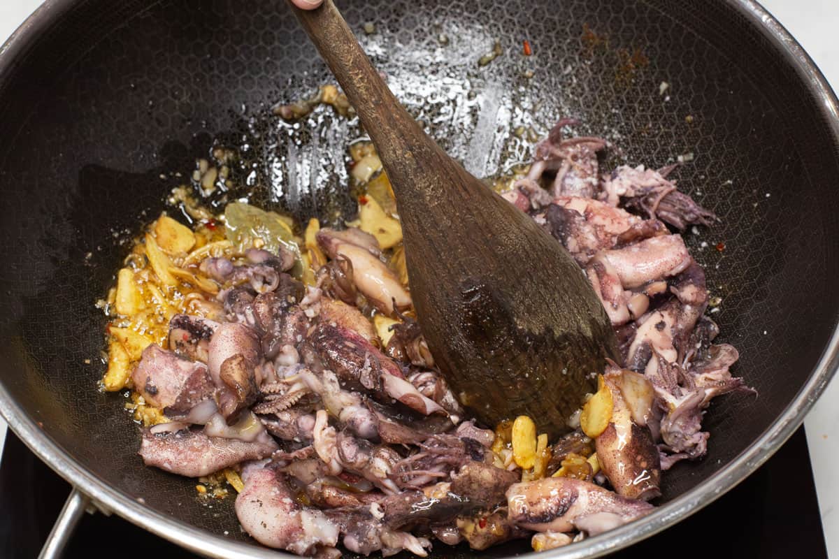 Tossing the squid with the aromatics and olive oil in a wok.