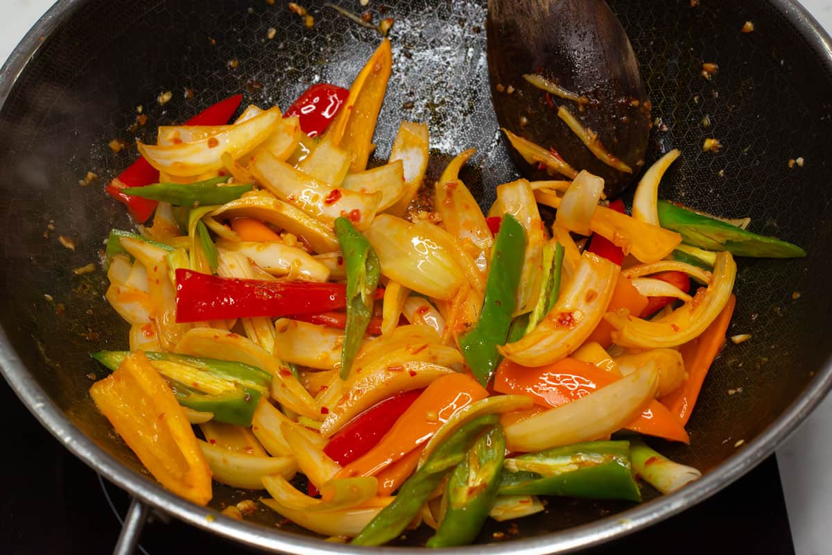 Mixing the aromatics and vegetables in a wok.
