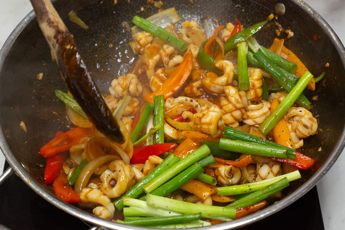 Mixing the Squid Stir fry in a wok with the green parts of the scallions.