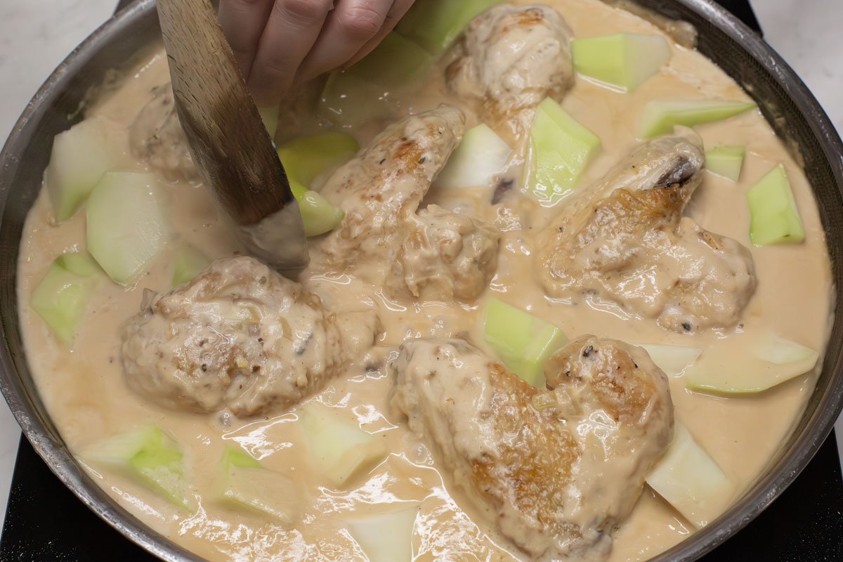adding green papaya to the chicken and coconut milk in the pan.