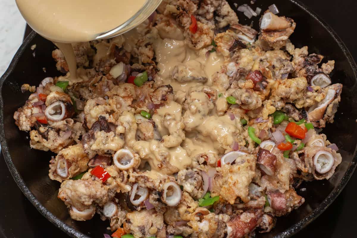 Pouring the sauce over the crispy squid and aromatics in the skillet.