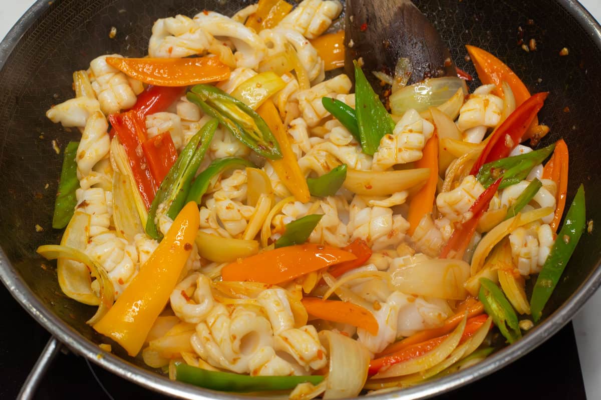 Mixing the squid with the vegetables in a wok.