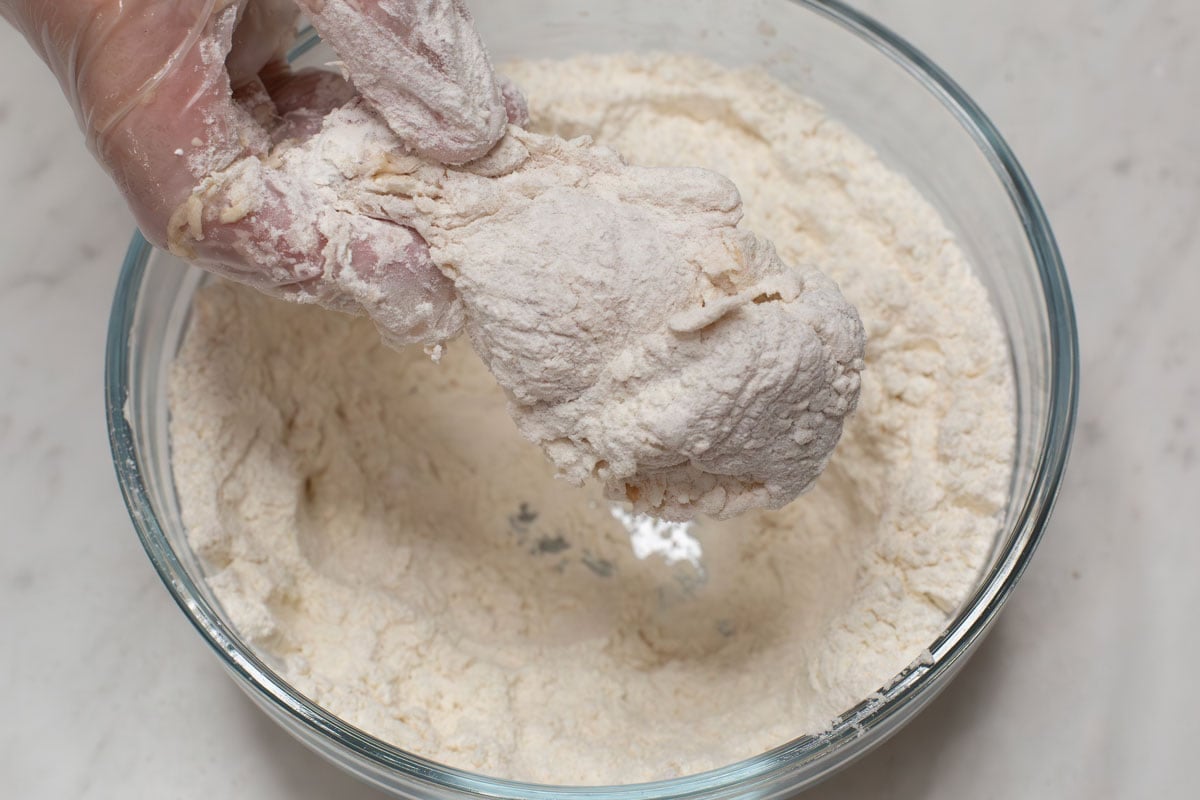Coating a piece of chicken in the flour mixture.