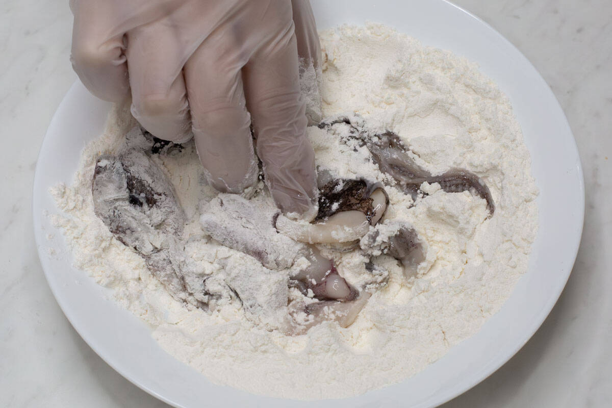 Coating the pieces of squid in a flour mixture.