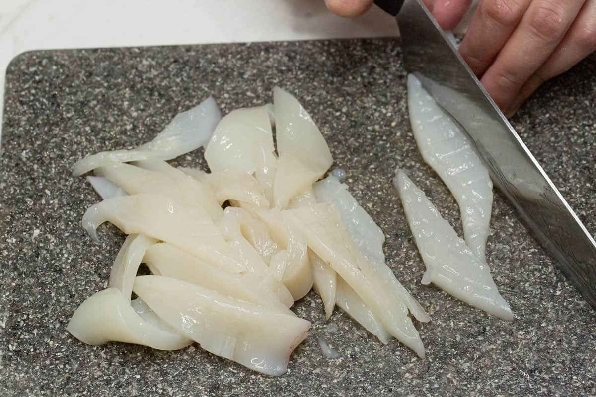 Slicing the squid body into strips on a cutting board.