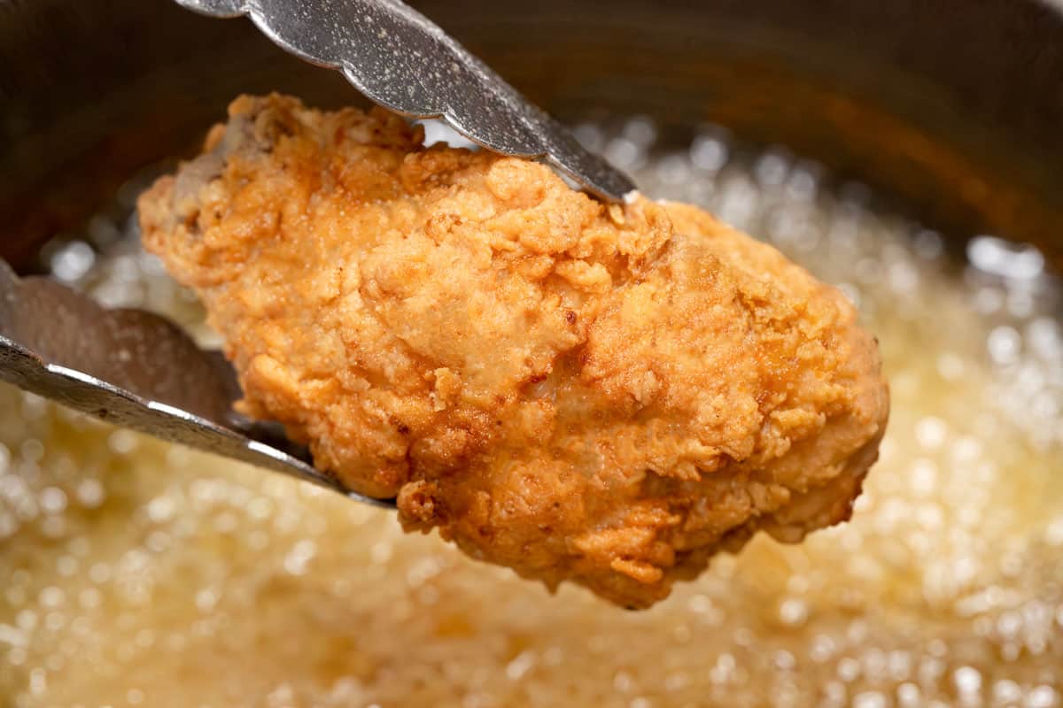 Holding chicken with tongs, fried the second time.