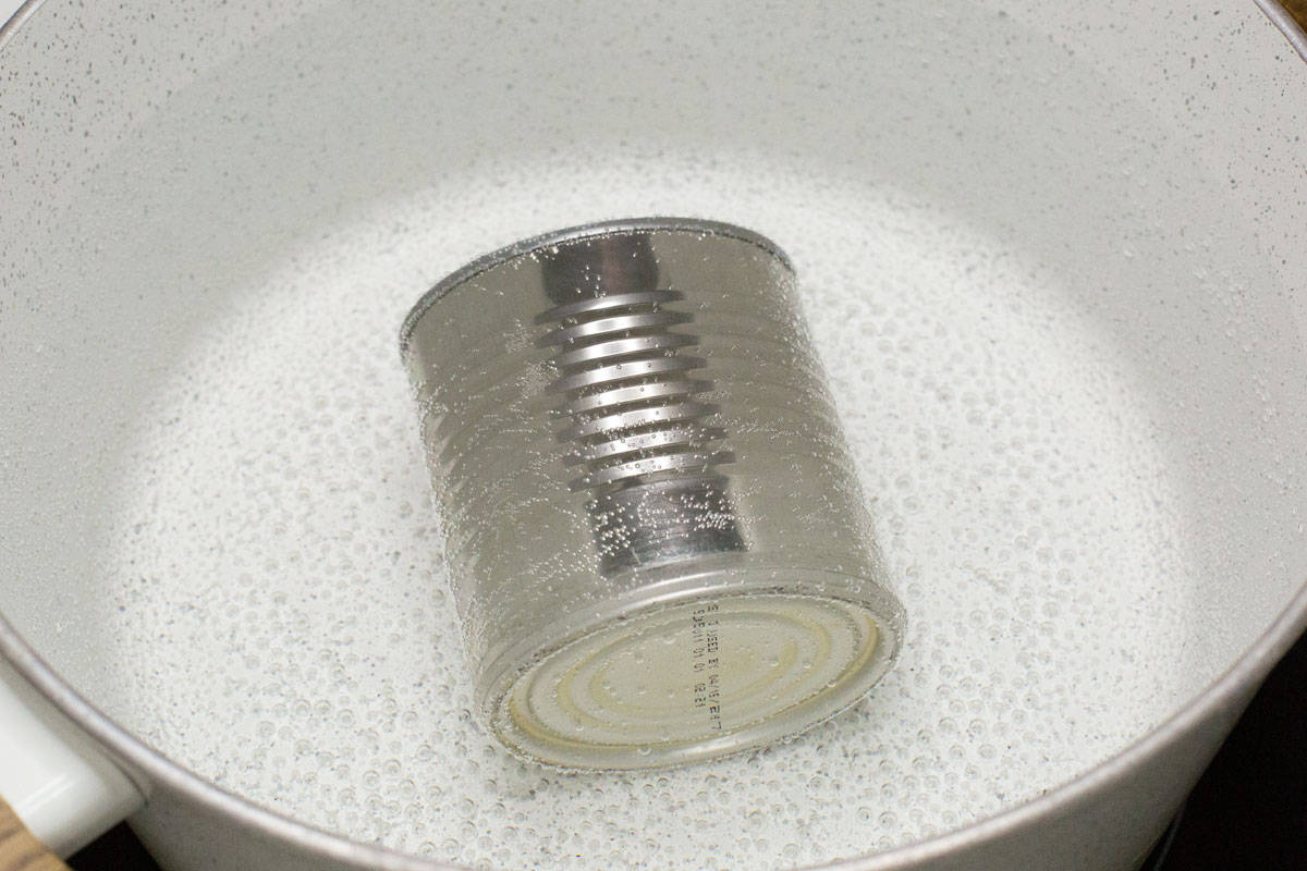 A can of condensed milk submerged in the simmering water in a pot.