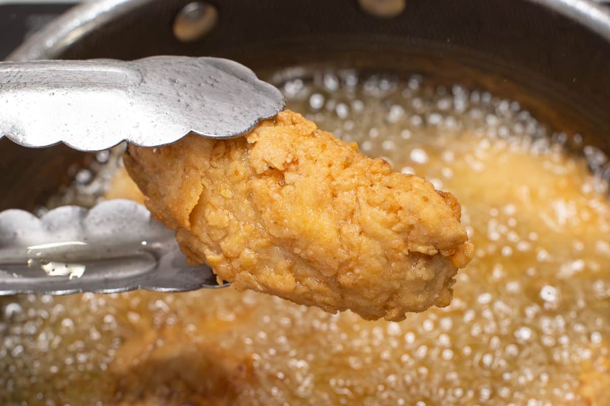 Holding a piece of chicken with tongs over the saucepan.