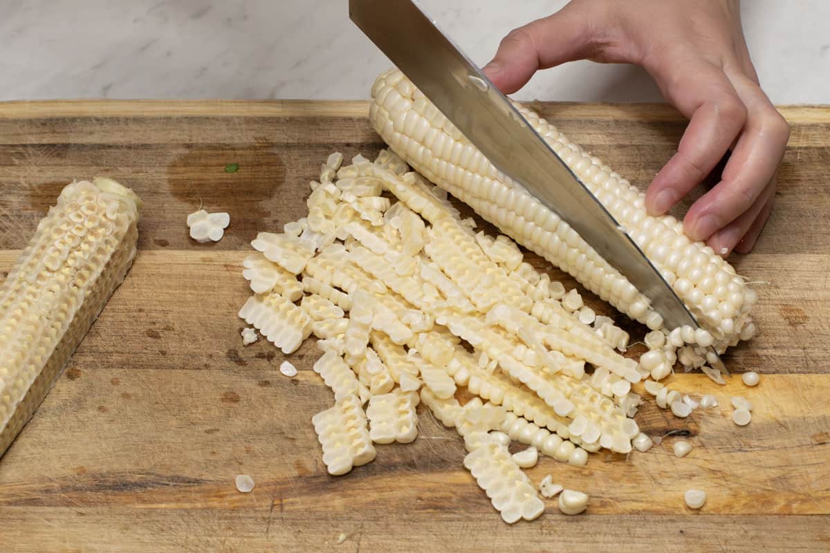 Slicing down one side of the corn on a cutting board.