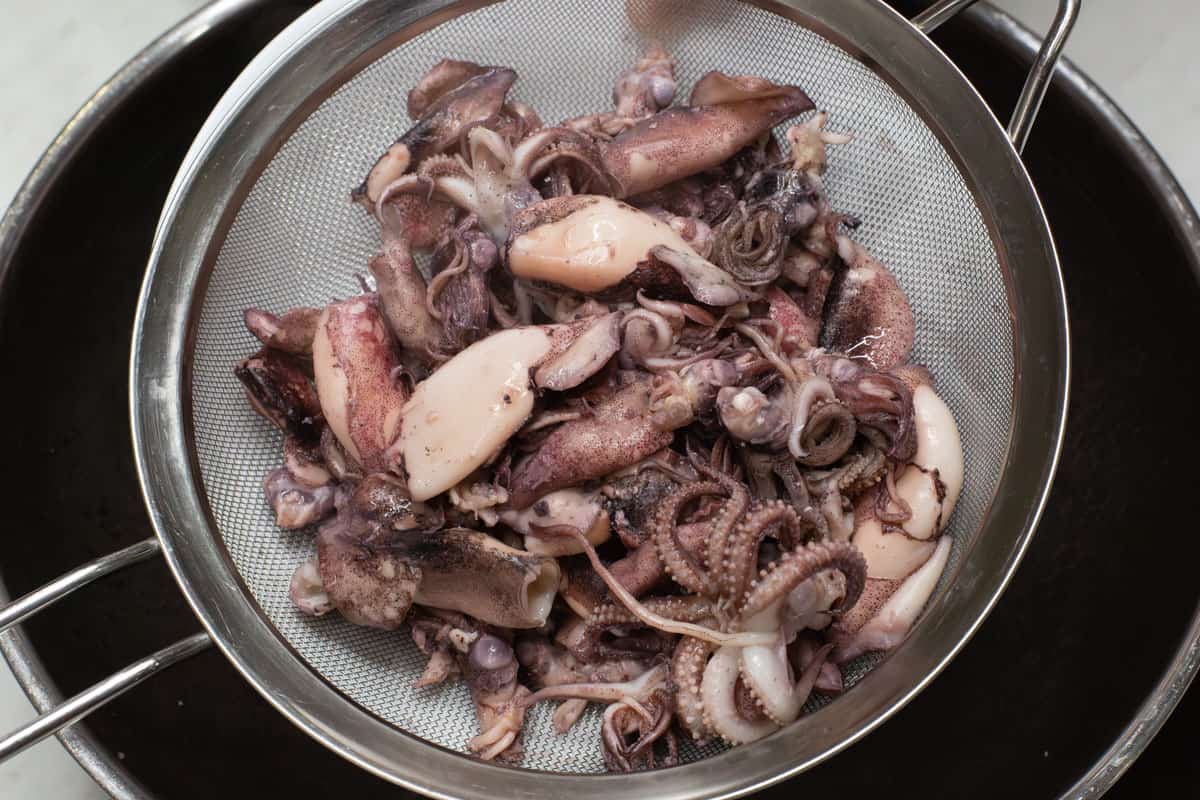 Straining the seared squid over a wok.