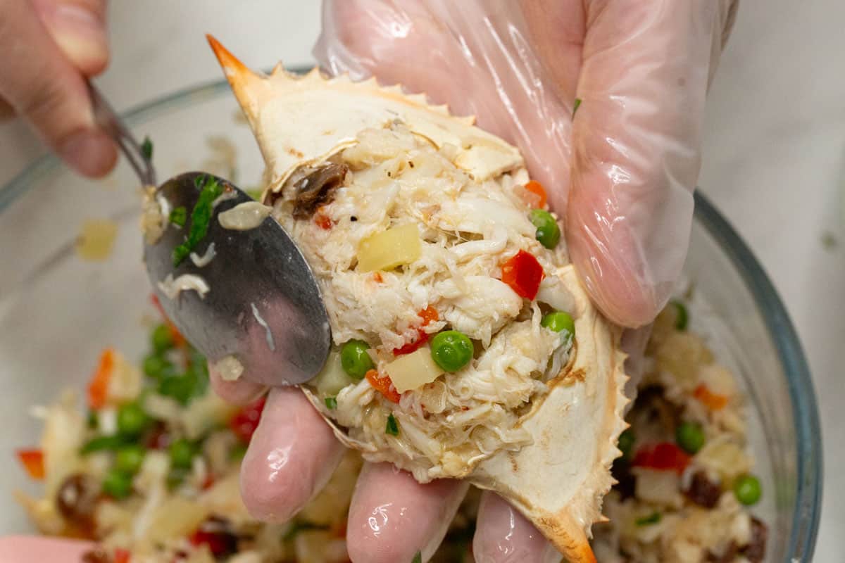 Stuffing the crab shells with the filling using a spoon.
