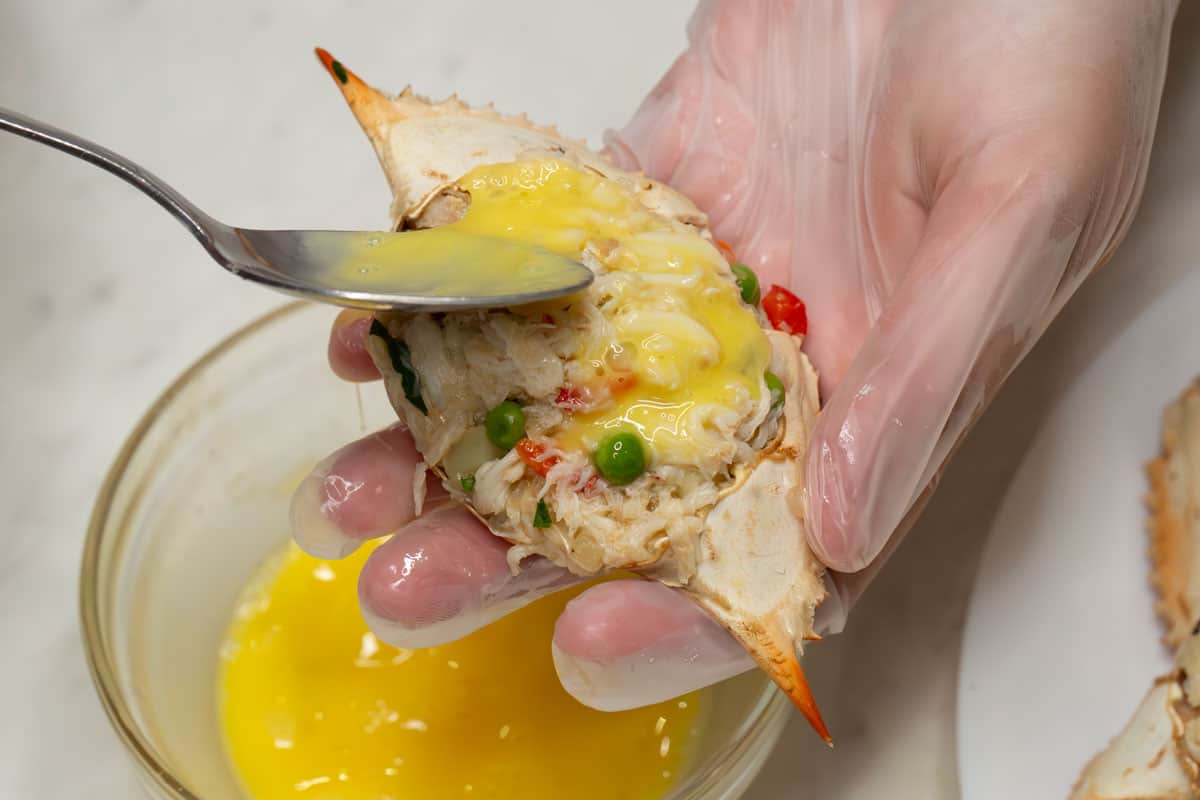 Pouring beaten egg over the crab mixture in the shell.