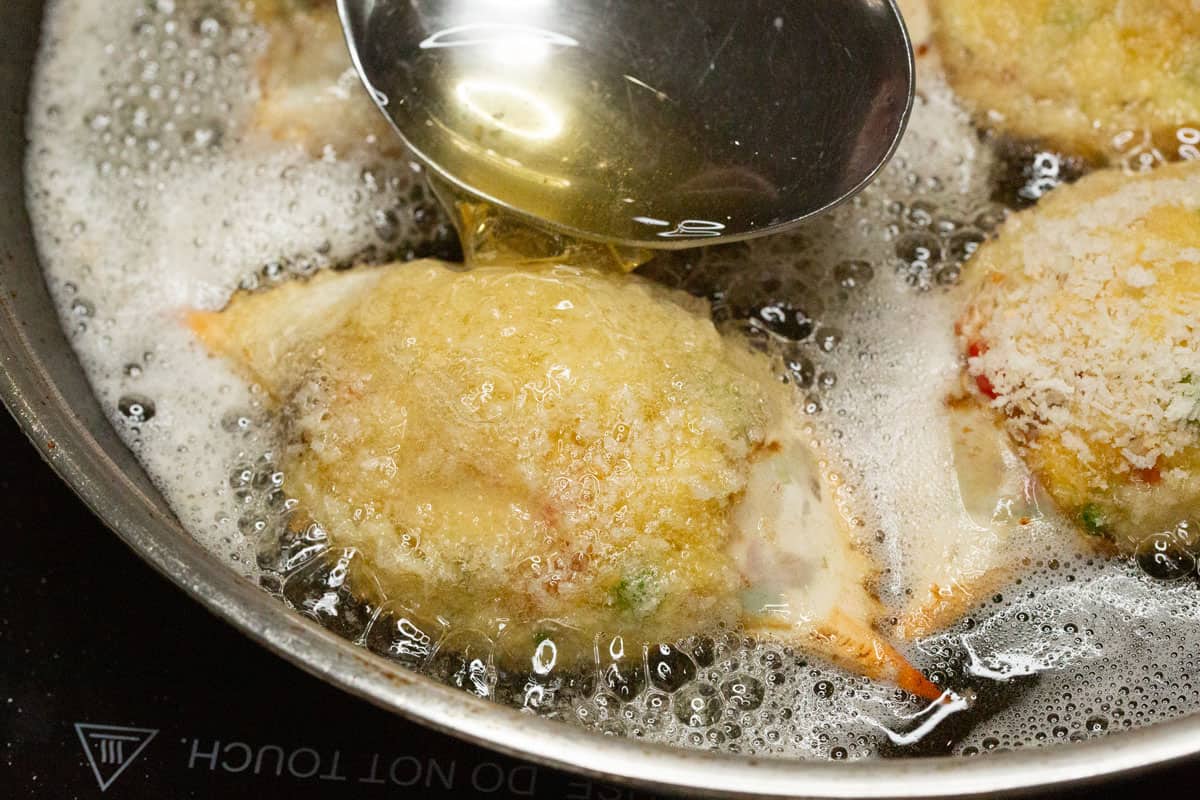 Spooning hot oil over the crab relleno while frying.
