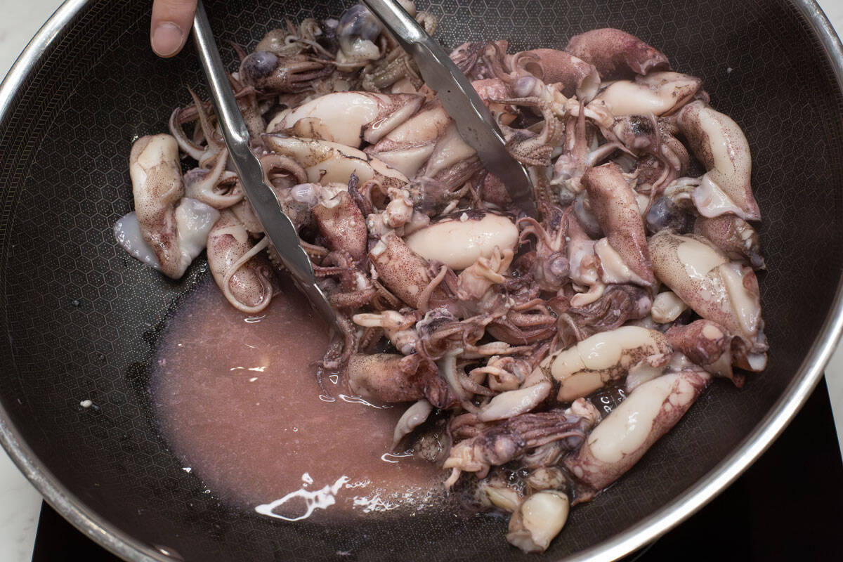 Seared squid with liquid in a wok.