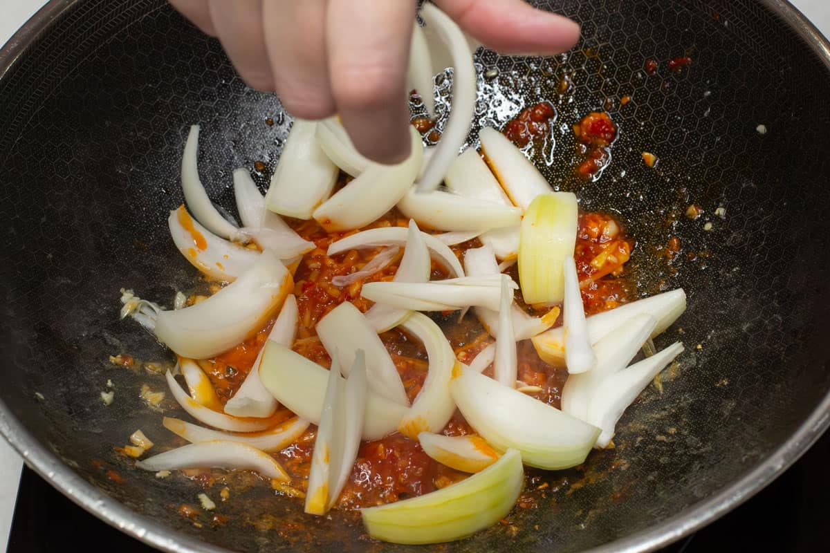 Adding the sliced onions to the aromatics in a wok.