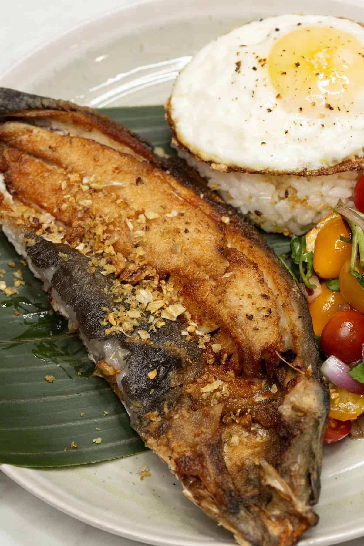Daing na Bangus with garlic rice, egg, and tomato salad on a plate.