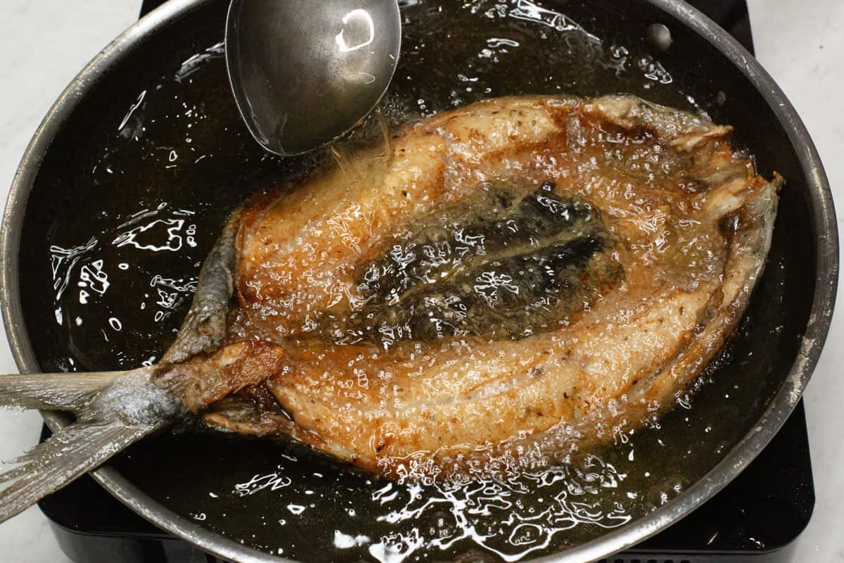 Spooning oil over the bangus using a ladle.