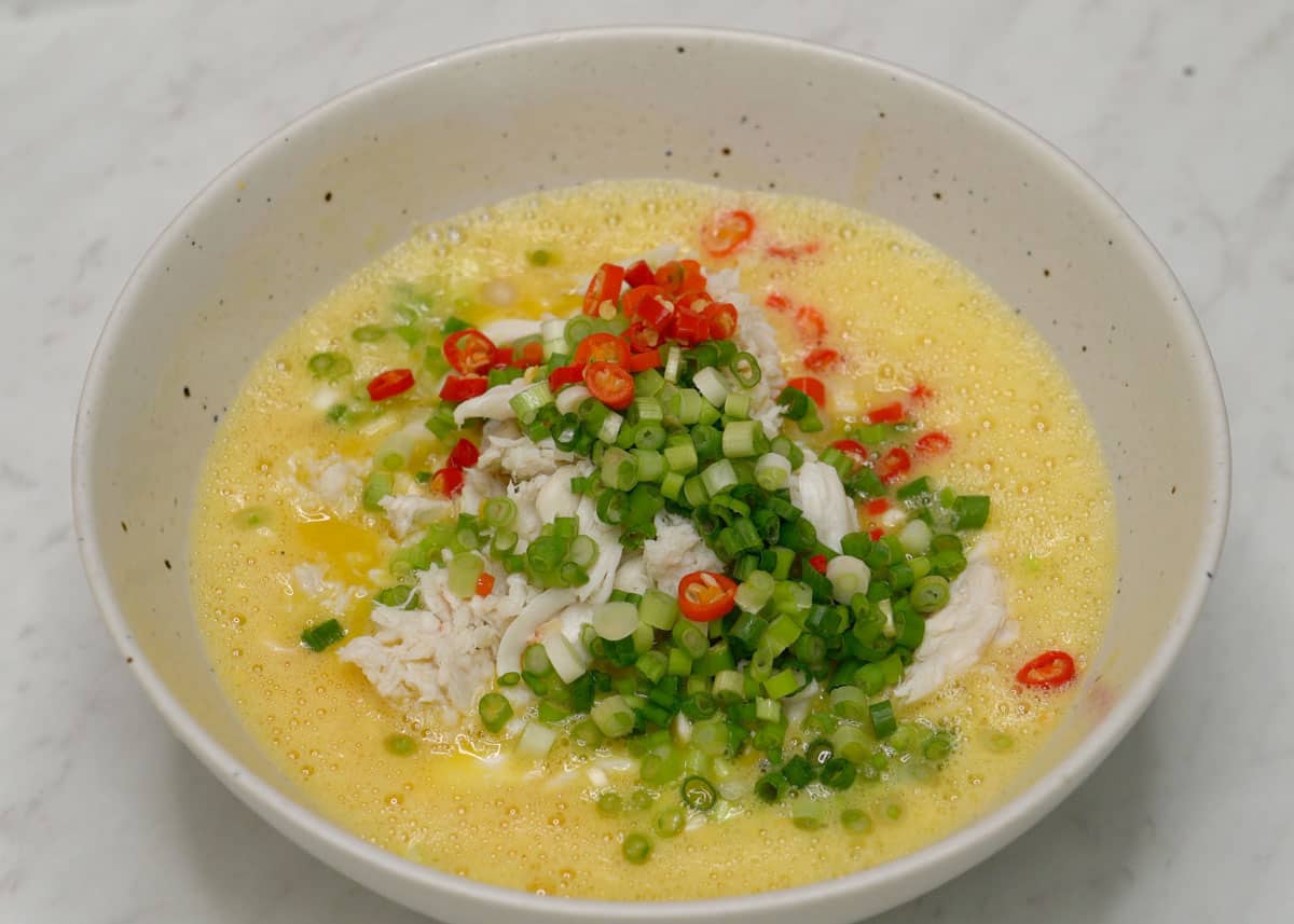 Beaten eggs with crab, scallions, and chilies in a bowl.