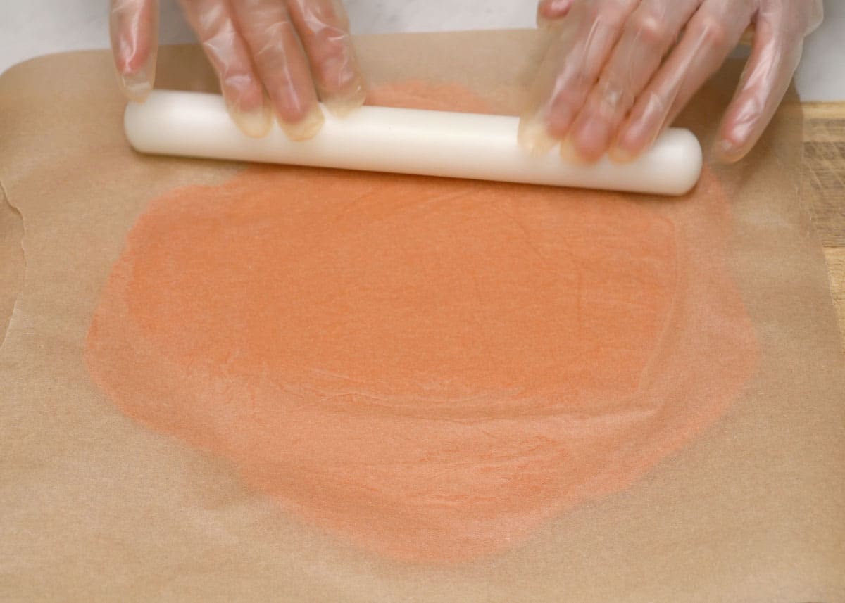 Rolling empanada dough between sheets of parchment paper.