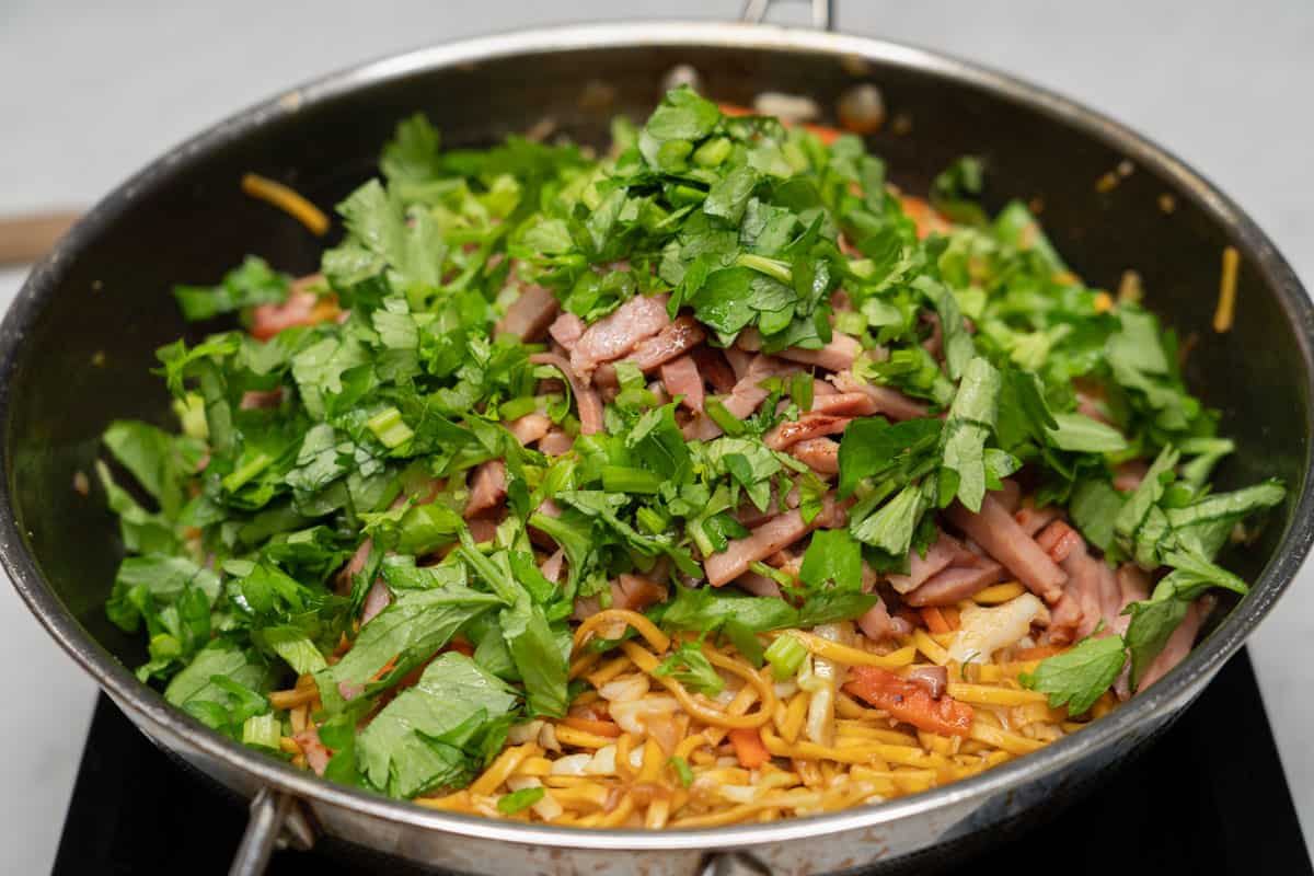 Chinese celery and ham added to the pancit canton noodles in a wok.