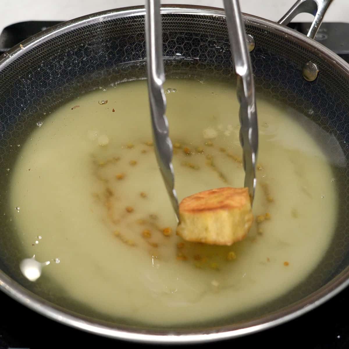 Adding sweet potato to caramelized sugar in hot oil.