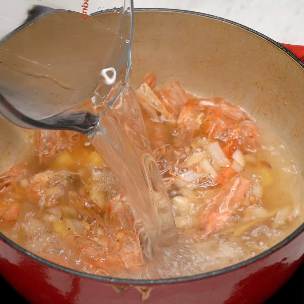 Adding water to the shrimps shells and aromatics in the pot.