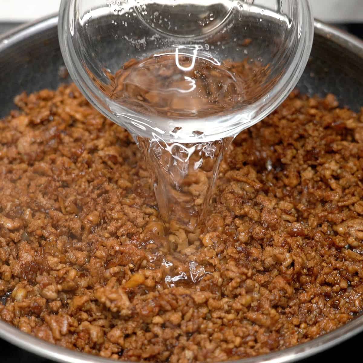 Adding water to the adobong giniling in the pan.