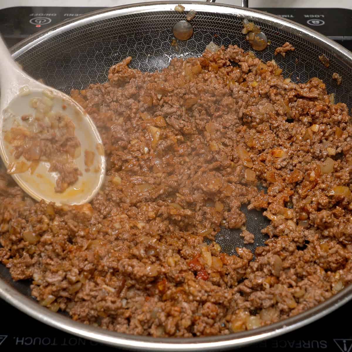 Cooking the tomato paste with the meat in a pan.