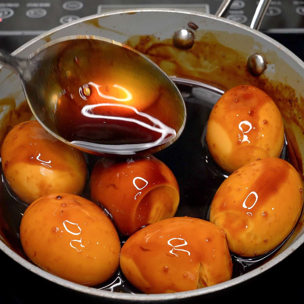 Spooning the adobo sauce over the eggs in a pan.