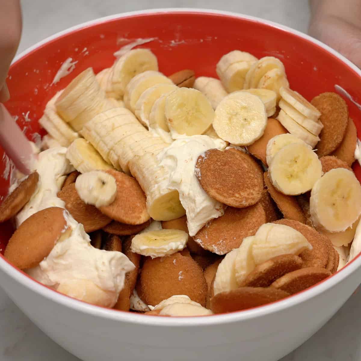Mixing the cream mixture, vanilla wafers, and sliced bananas in a bowl.