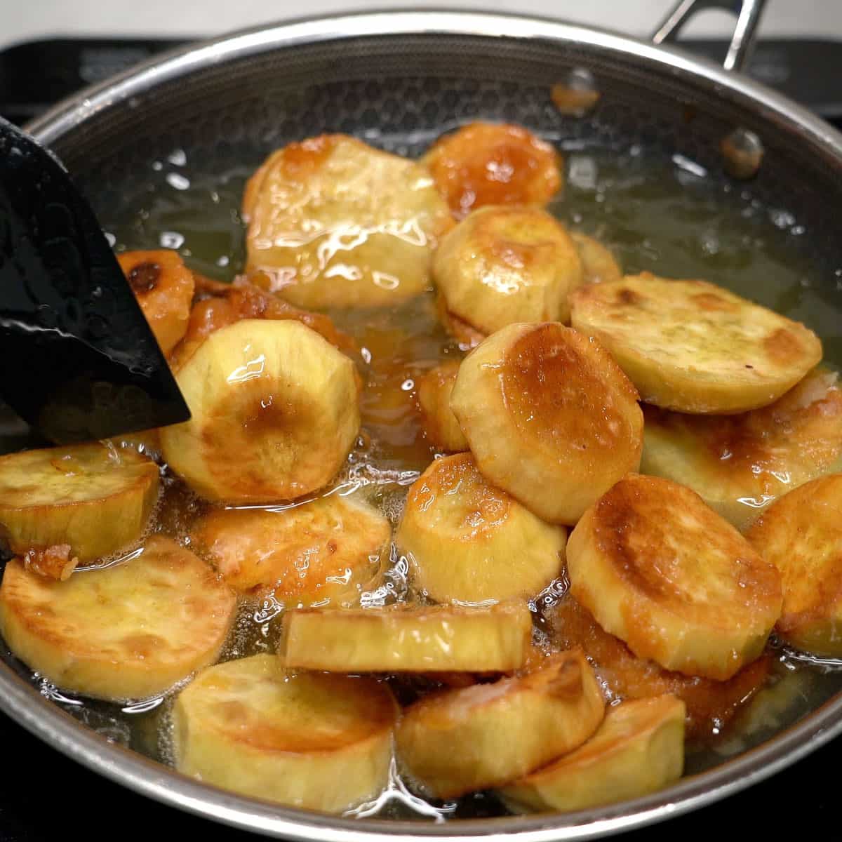 Sweet potatoes in the oil while suagr is caramelizeng.