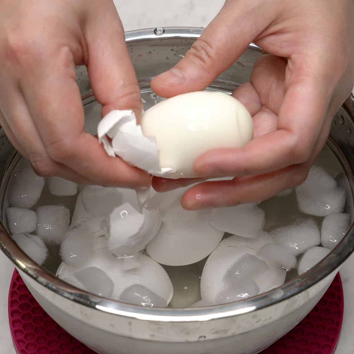 Peeling eggs over a bowl with eggs in ice water.