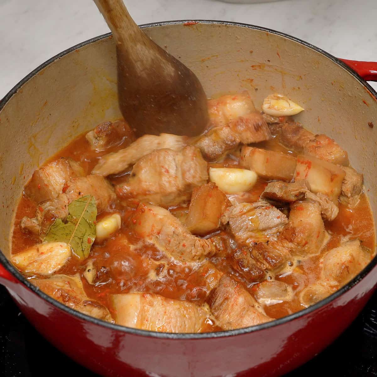Mixing adobong pula in a pot.