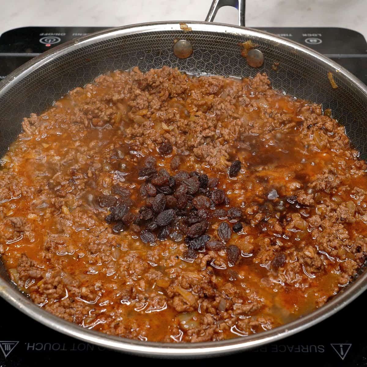 Raisins and other seasonings with the ground meat in a pan.