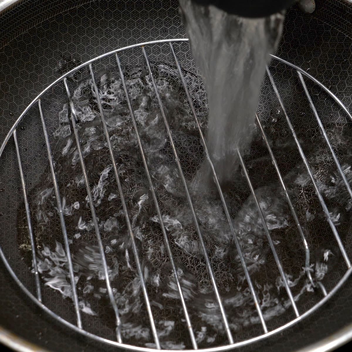 Pouring water over the rack in a wok.