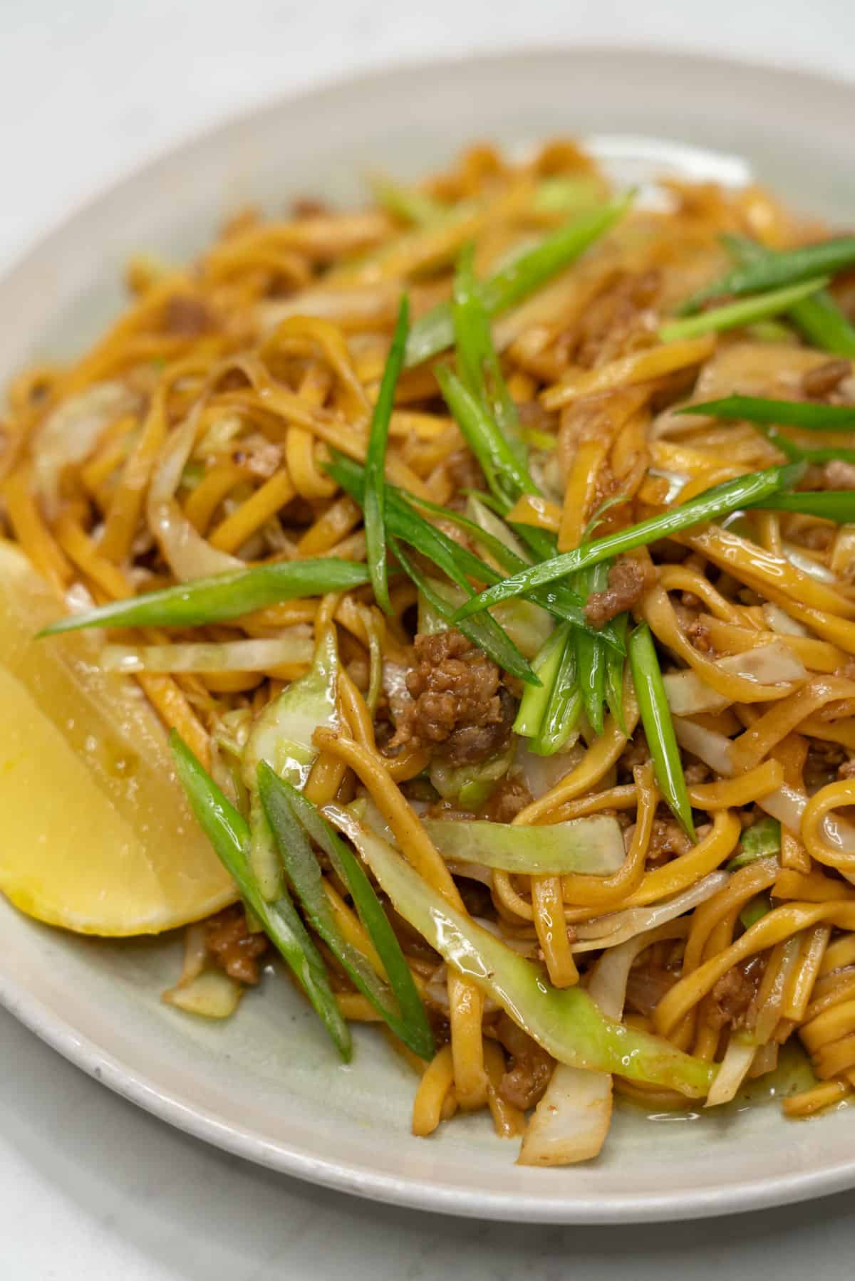 Pancit canton with ground pork and cabbage on a plate with lemon and scallions.