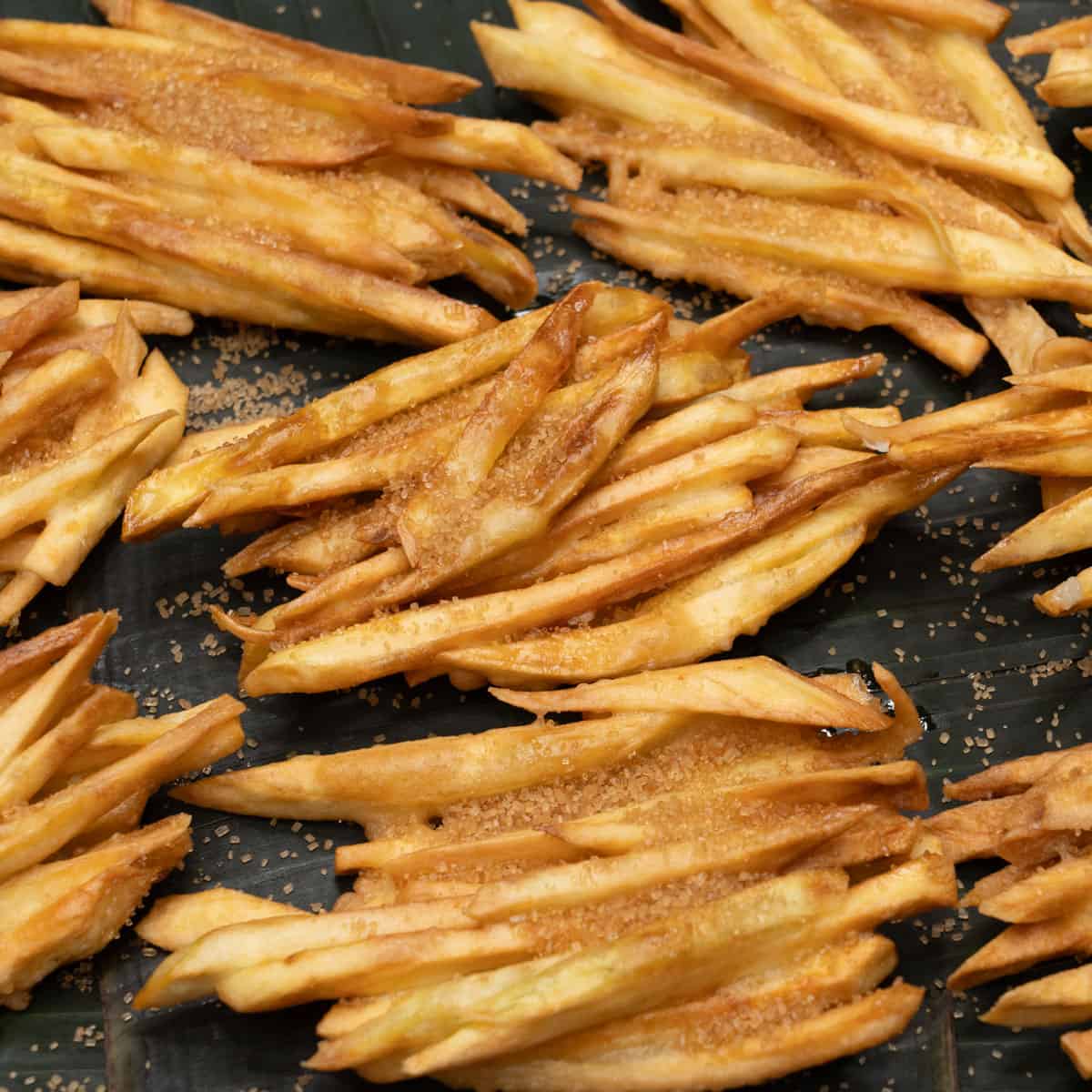 Sweet potato fritters with sugar on banana leaves.