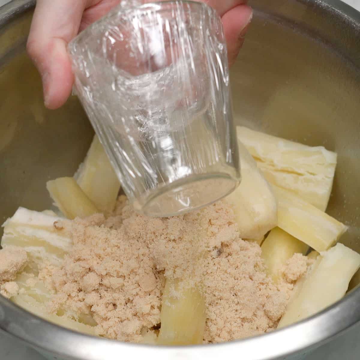 Holding a glass over a bowl with cassava and sugar.