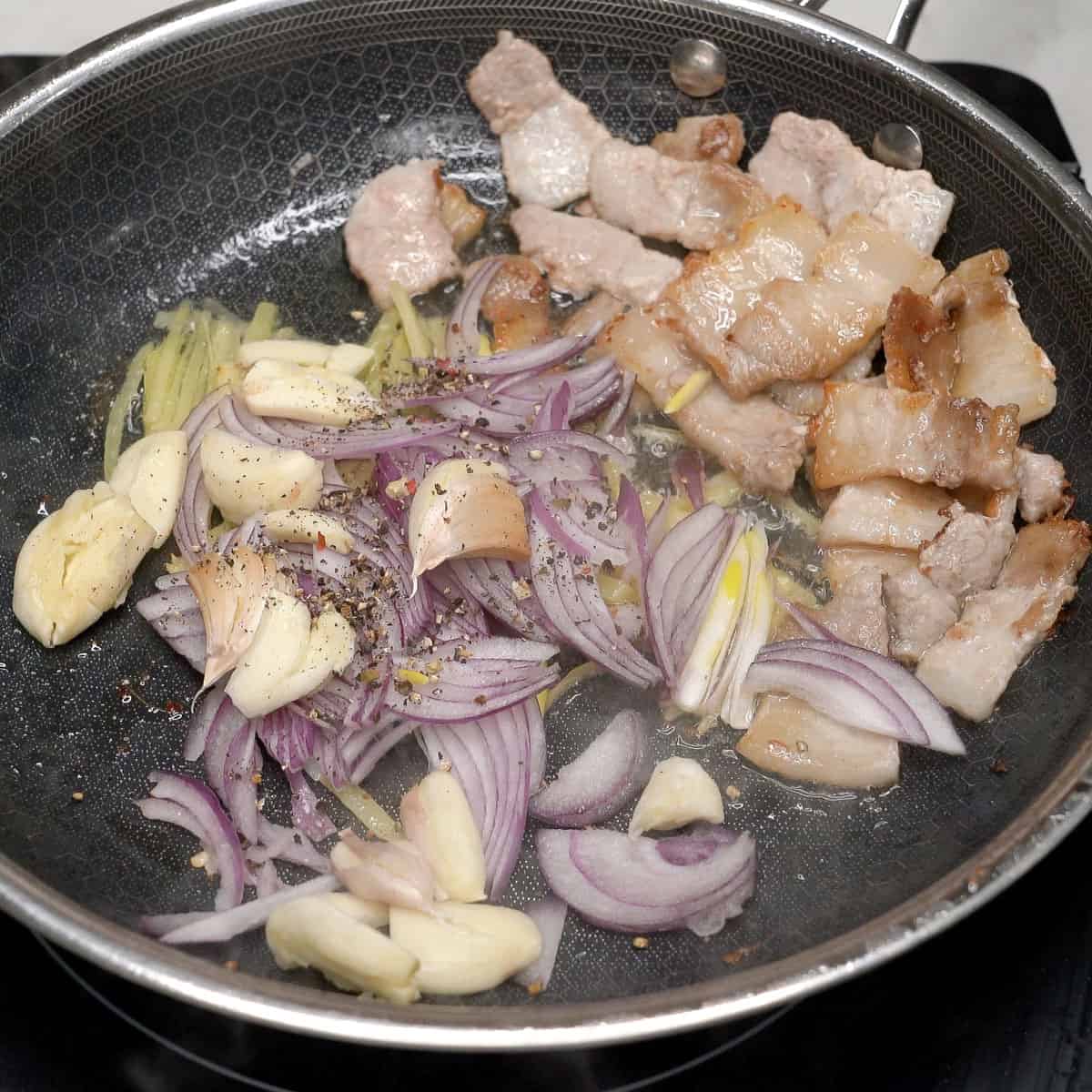 Browned pork with aromatics in a pan.