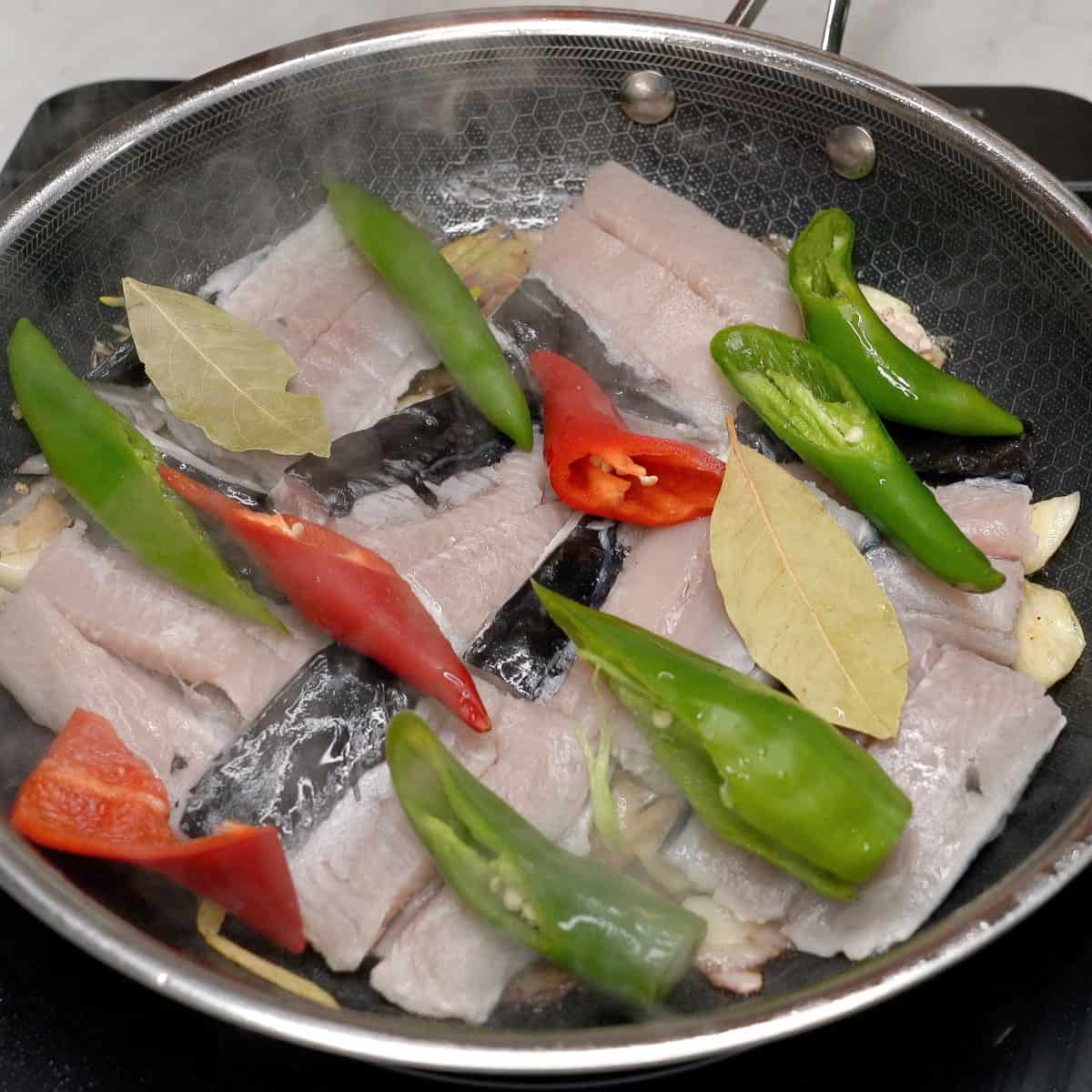 Bangus with chilies and other ingredients for adobo in the pan.